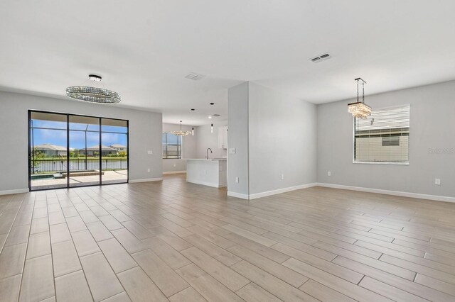 unfurnished living room featuring baseboards, visible vents, a sink, and an inviting chandelier