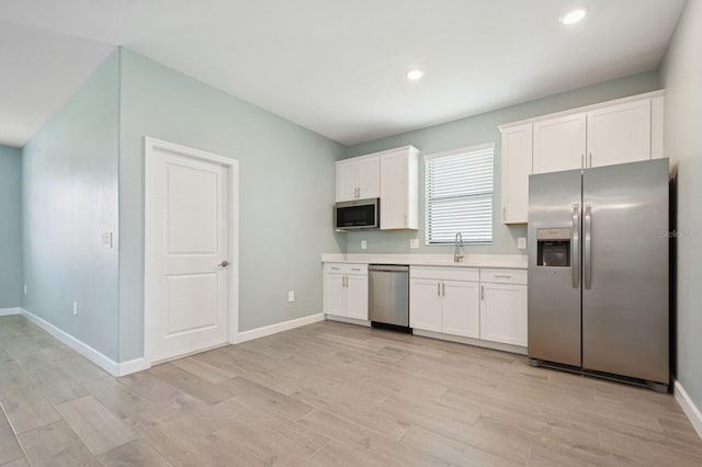 kitchen featuring light wood-style floors, white cabinets, light countertops, stainless steel appliances, and baseboards