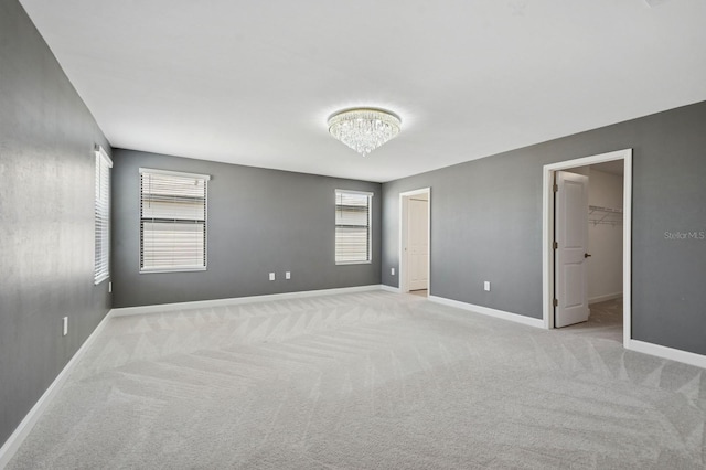 carpeted spare room with an inviting chandelier and baseboards