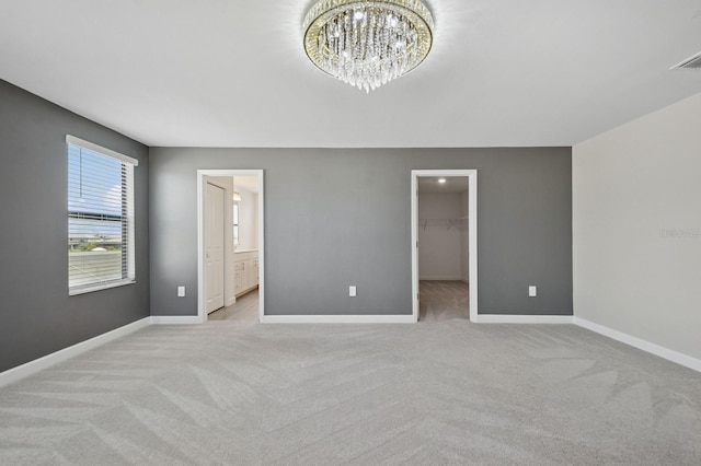 unfurnished bedroom with light carpet, a notable chandelier, a spacious closet, and baseboards