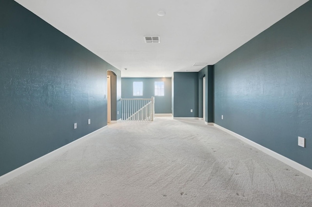 carpeted spare room with visible vents, baseboards, and arched walkways