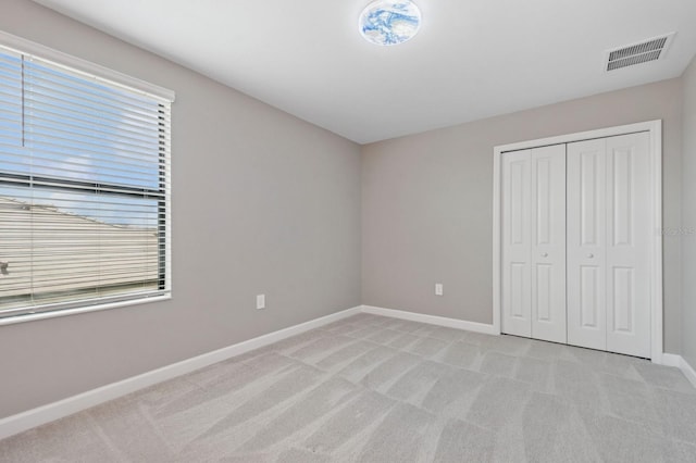 unfurnished bedroom featuring visible vents, baseboards, a closet, and light carpet