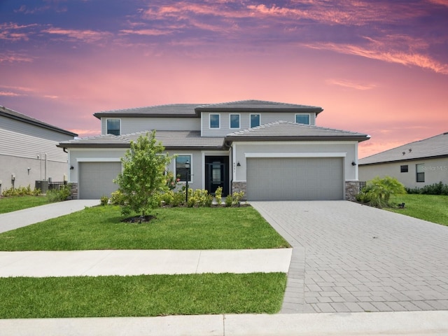 prairie-style home with an attached garage, a lawn, stone siding, and decorative driveway