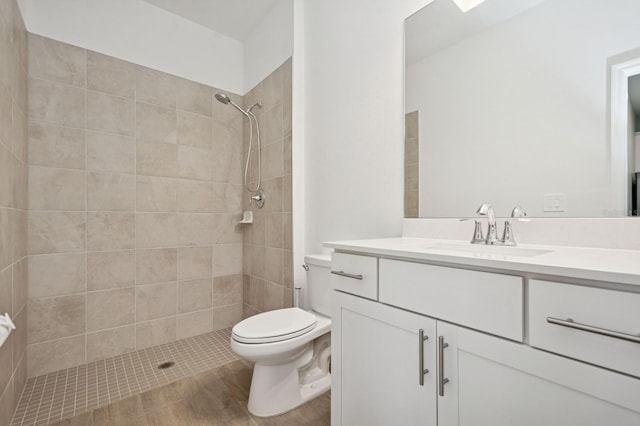 full bath featuring wood finished floors, a tile shower, vanity, and toilet