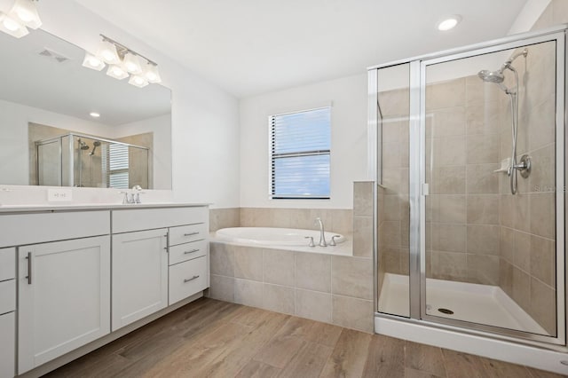 bathroom with a shower stall, wood finished floors, visible vents, vanity, and a garden tub