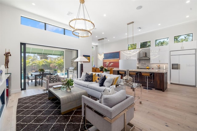 living area with light wood finished floors, a healthy amount of sunlight, a towering ceiling, recessed lighting, and a notable chandelier