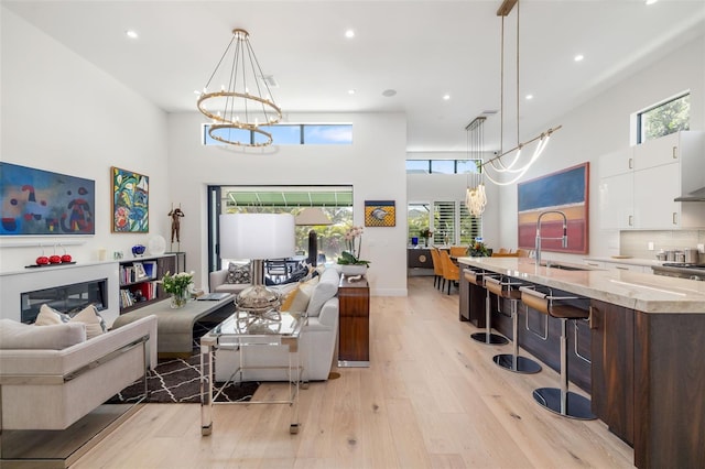 living area with a chandelier, a high ceiling, light wood finished floors, and recessed lighting