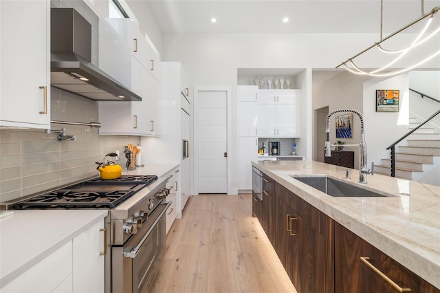 kitchen featuring high end stainless steel range, light wood finished floors, a sink, modern cabinets, and wall chimney range hood