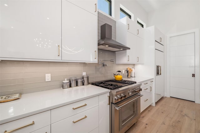 kitchen featuring white cabinets, stainless steel stove, tasteful backsplash, and wall chimney exhaust hood