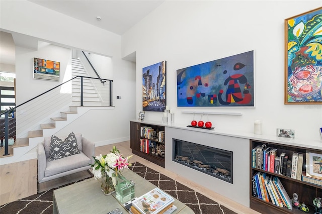 living room with stairway, baseboards, a glass covered fireplace, and wood finished floors