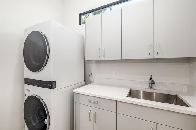 laundry area with cabinet space, stacked washer / drying machine, and a sink