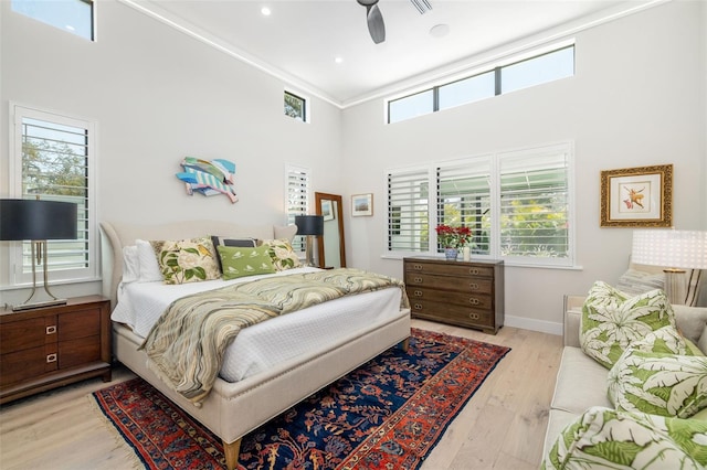 bedroom featuring baseboards, a high ceiling, ceiling fan, and light wood-style flooring