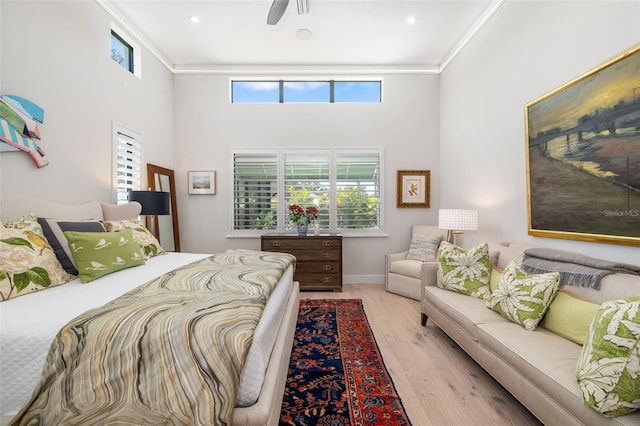 bedroom featuring light wood finished floors, baseboards, a towering ceiling, and crown molding