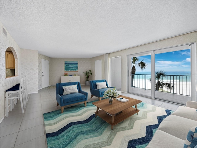 living room with a textured ceiling, tile patterned floors, wallpapered walls, a water view, and baseboards