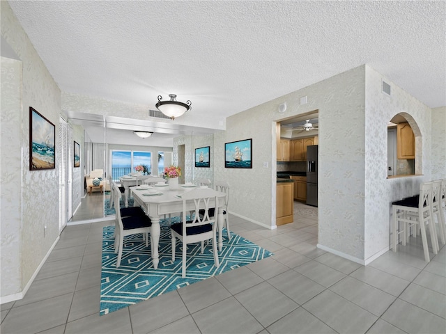 dining area with wallpapered walls, light tile patterned flooring, baseboards, a textured ceiling, and ceiling fan