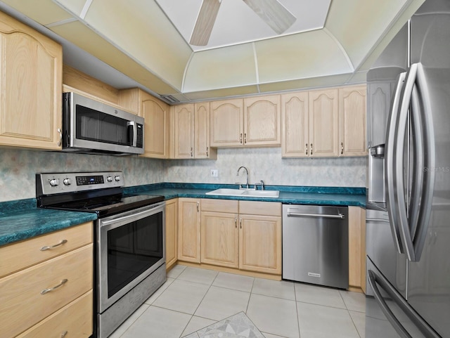 kitchen featuring appliances with stainless steel finishes, a sink, light brown cabinets, and dark countertops