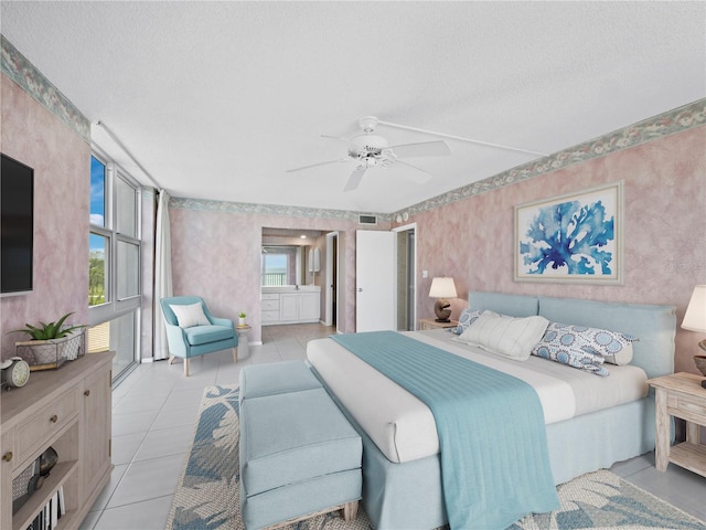 bedroom featuring wallpapered walls, light tile patterned floors, a textured ceiling, ensuite bath, and a ceiling fan