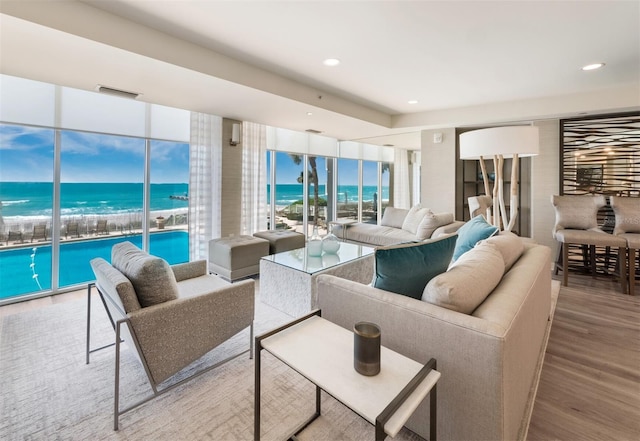 living room featuring wood finished floors, view of water and beach, and recessed lighting