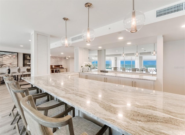 kitchen featuring light stone counters, light wood-style floors, a kitchen breakfast bar, recessed lighting, and decorative light fixtures