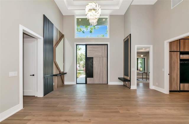 entrance foyer with wood finished floors, a high ceiling, a notable chandelier, and a tray ceiling