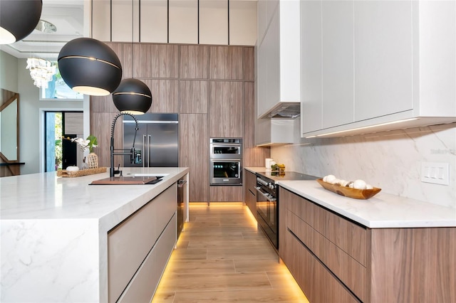 kitchen featuring a sink, light wood-type flooring, modern cabinets, a center island with sink, and appliances with stainless steel finishes
