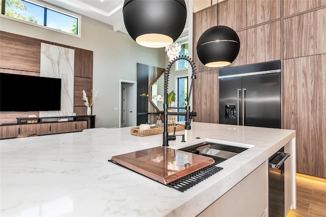 kitchen featuring light stone countertops, modern cabinets, stainless steel built in fridge, and a high ceiling