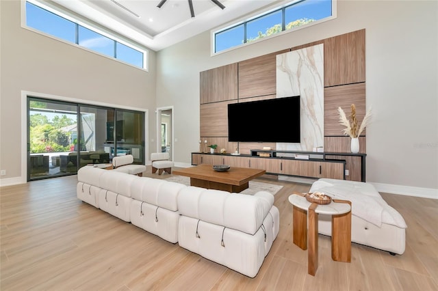living area featuring baseboards, a towering ceiling, and light wood-type flooring