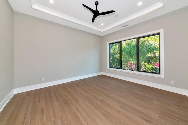 spare room with visible vents, a ceiling fan, a tray ceiling, and wood finished floors
