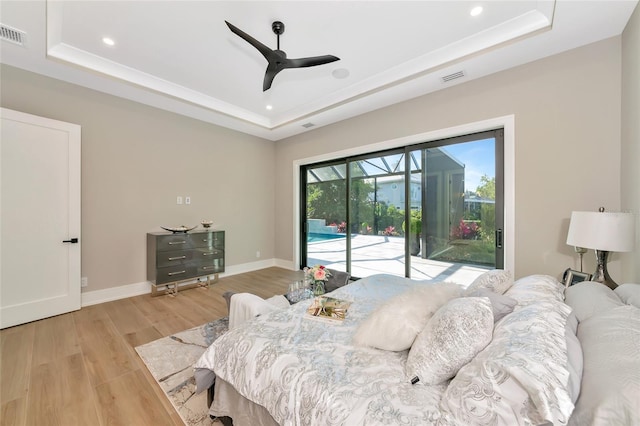 bedroom with a sunroom, light wood-style floors, a raised ceiling, and access to exterior