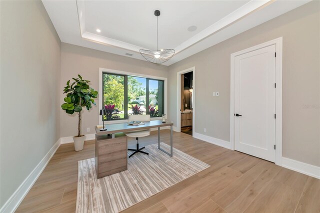 office area featuring baseboards, a tray ceiling, and light wood-style flooring