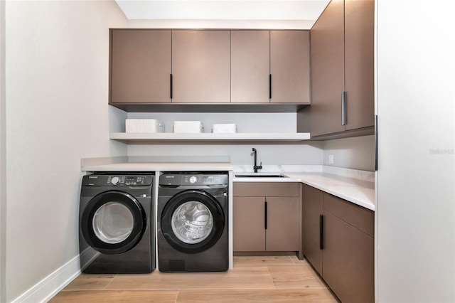 clothes washing area featuring a sink, cabinet space, light wood-style flooring, washing machine and dryer, and baseboards