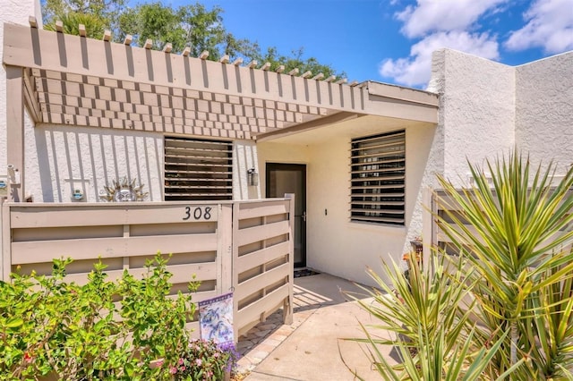 view of exterior entry with stucco siding and fence