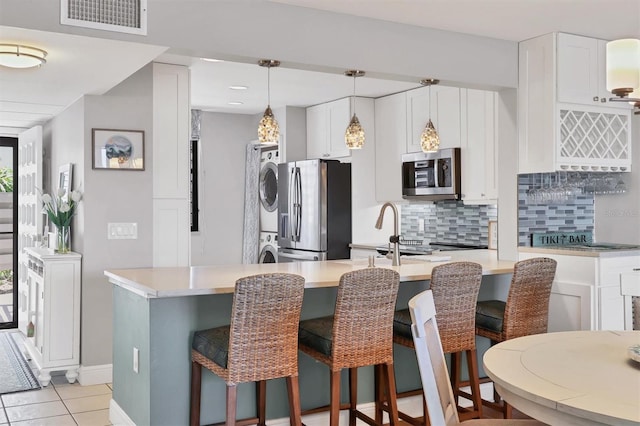 kitchen featuring a kitchen breakfast bar, stacked washer / drying machine, stainless steel appliances, backsplash, and visible vents
