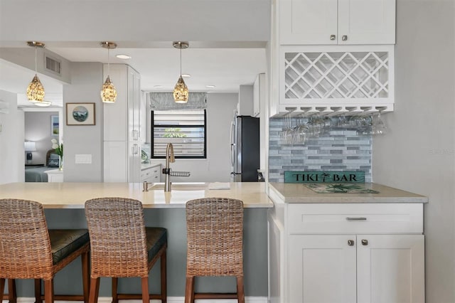 kitchen with white cabinets, a kitchen breakfast bar, a sink, freestanding refrigerator, and decorative backsplash