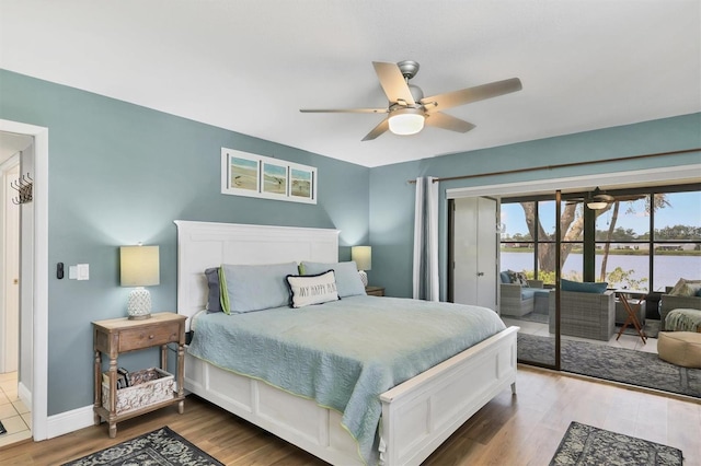 bedroom with wood finished floors, a water view, baseboards, access to outside, and ceiling fan