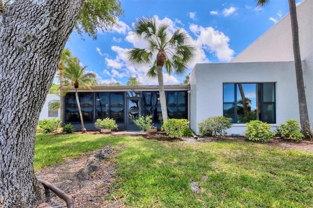 back of property featuring a yard, a sunroom, and stucco siding