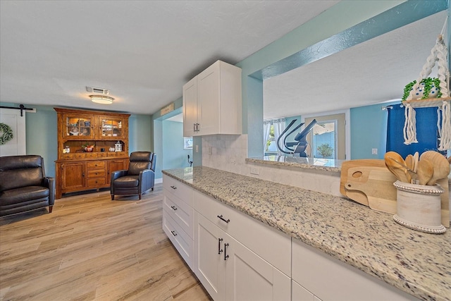 130 E Seminole Dr, Venice, FL 34293 - kitchen with light stone countertops, light wood-style flooring, white cabinetry, visible vents, and a barn door