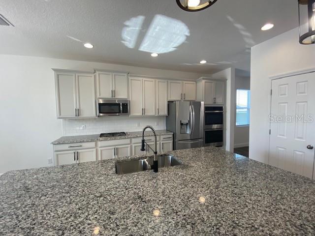 1142 Blarney St, Minneola, FL 34715 - kitchen with tasteful backsplash, a sink, appliances with stainless steel finishes, recessed lighting, and dark stone counters