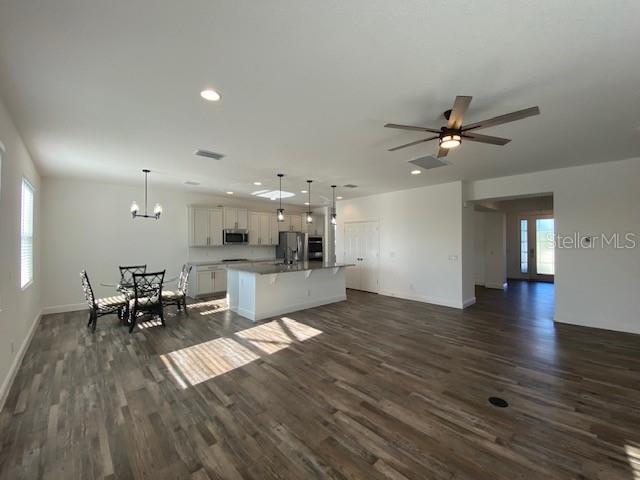 1142 Blarney St, Minneola, FL 34715 - kitchen featuring white cabinets, appliances with stainless steel finishes, dark wood-style flooring, open floor plan, and a center island with sink