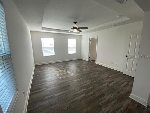 1142 Blarney St, Minneola, FL 34715 - empty room featuring a tray ceiling, visible vents, dark wood-type flooring, baseboards, and ceiling fan