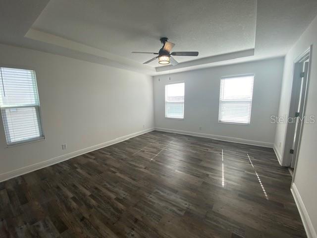 1142 Blarney St, Minneola, FL 34715 - spare room with dark wood-style floors, a tray ceiling, baseboards, and ceiling fan