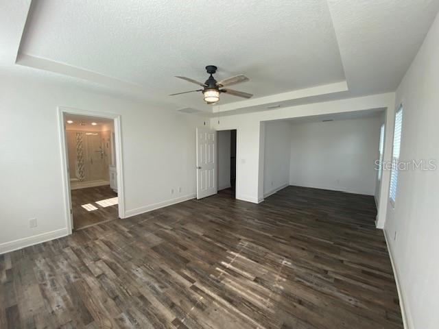 1142 Blarney St, Minneola, FL 34715 - unfurnished bedroom with dark wood-style floors, a tray ceiling, baseboards, a textured ceiling, and ceiling fan