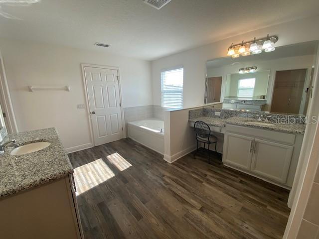 1142 Blarney St, Minneola, FL 34715 - full bathroom with wood finished floors, two vanities, a sink, and a garden tub