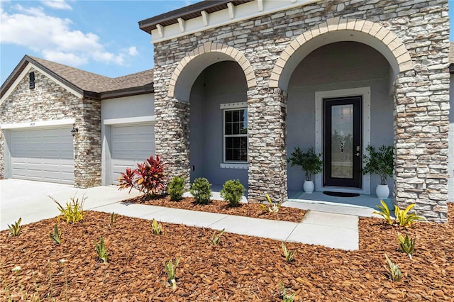 doorway to property featuring concrete driveway, an attached garage, and stone siding