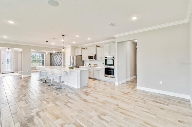 kitchen featuring stainless steel appliances, light countertops, ornamental molding, baseboards, and a center island with sink