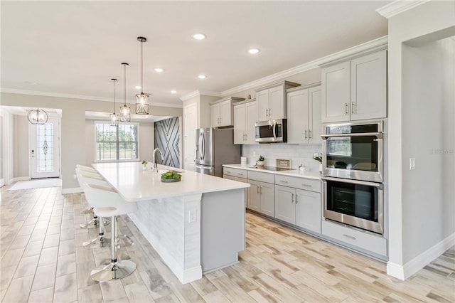 kitchen featuring an island with sink, stainless steel appliances, light countertops, backsplash, and a sink