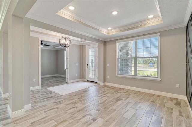 empty room with ornamental molding, an inviting chandelier, a raised ceiling, and light wood-style floors