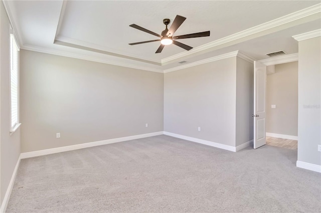 carpeted spare room with ceiling fan, a raised ceiling, visible vents, baseboards, and ornamental molding