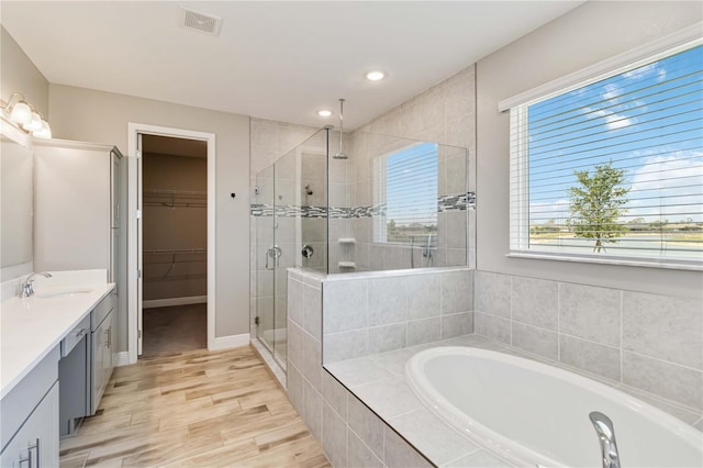 bathroom featuring a shower stall, vanity, a walk in closet, a garden tub, and wood finished floors