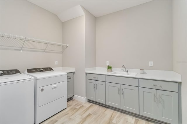 clothes washing area with washer and dryer, cabinet space, light wood finished floors, a sink, and baseboards